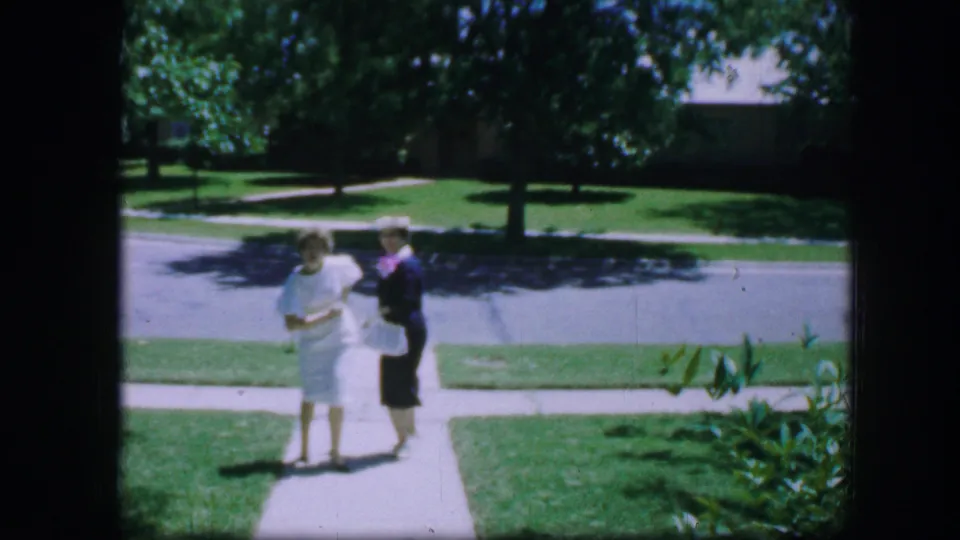 The two women face the camera on a Fort Worth sidewalk, with the woman in white beside the woman in a dark dress and hat.