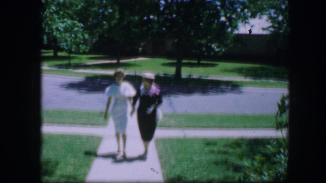 Two women in formal dresses walk hand-in-hand on a suburban sidewalk.