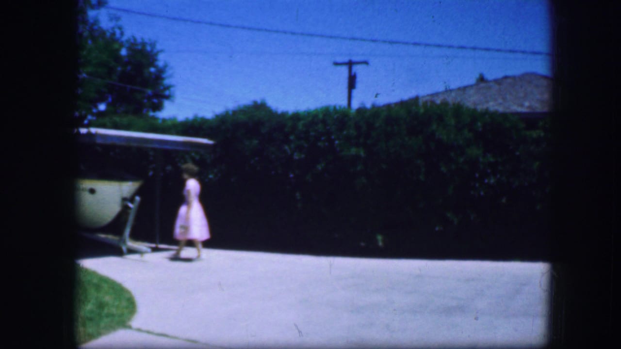 Woman continues walking along the driveway toward a covered structure.