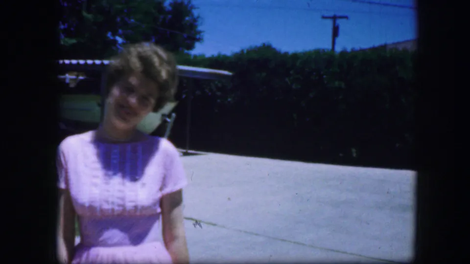 Close home-movie view of the woman in a pink dress, apparently smiling toward the camera in a Fort Worth suburban driveway.