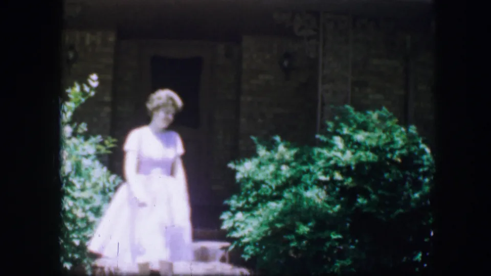 A woman in a pale white dress walks down stone steps in a landscaped Fort Worth setting in 1964 8mm footage.