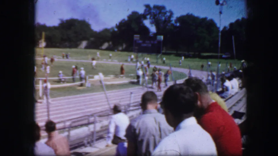 A home-movie frame shows spectators in bleachers looking toward a sports field, likely from the same Fort Worth 1964 reel.
