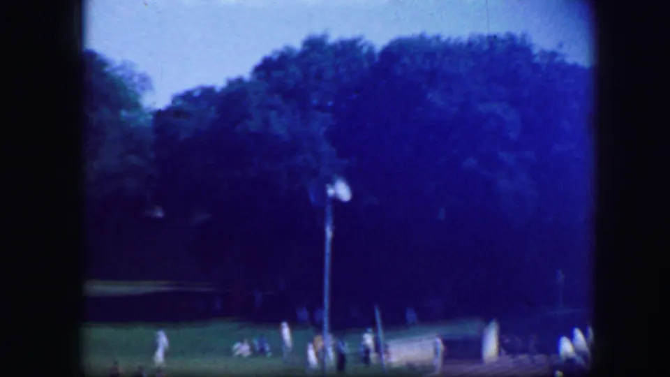 Fort Worth 1964 frame with a distant field view, trees, and small figures gathered near a low barrier.