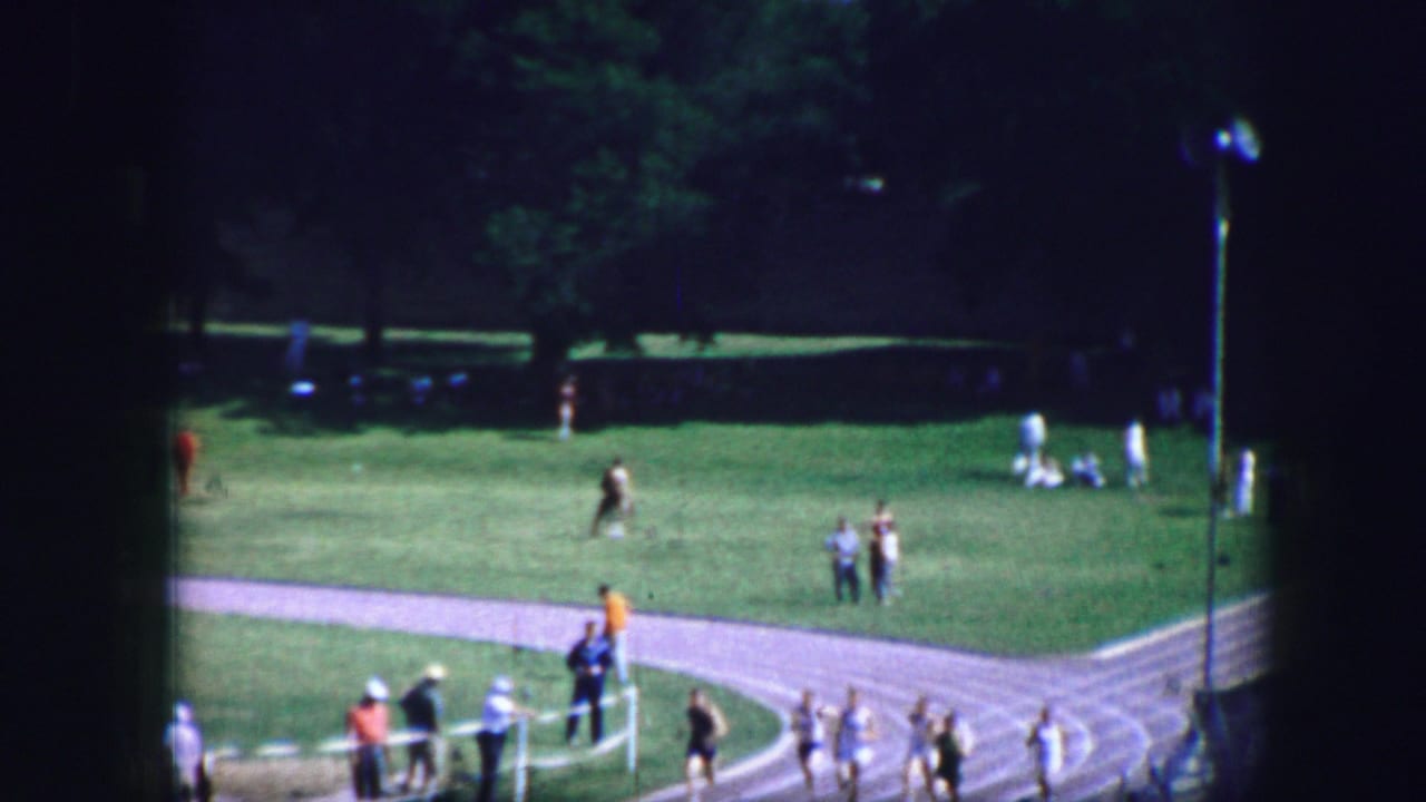 Runners continue along the curve with scattered spectators and groups on the grass field.