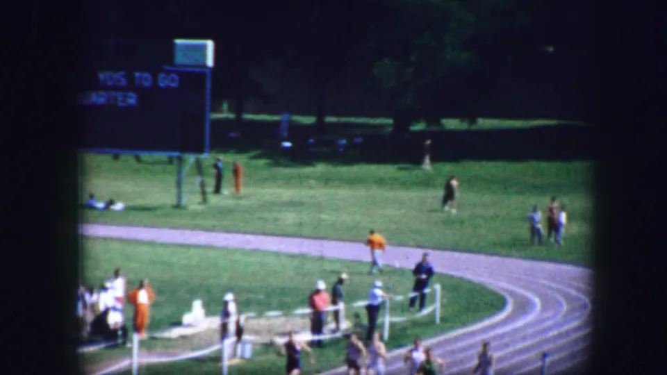 1964 Fort Worth outdoor track meet view showing a scoreboard, grassy field, spectators, and runners near the curve.