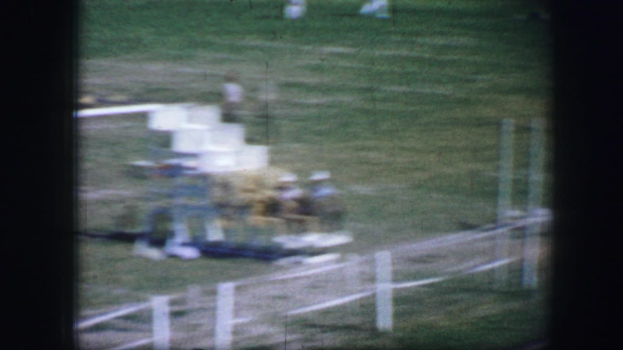 Blurred finish-area view with people near a white fence on grass.