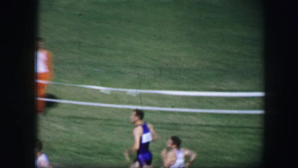 1964 Fort Worth home-movie frame showing a runner in a dark uniform passing near white rails on the grass.