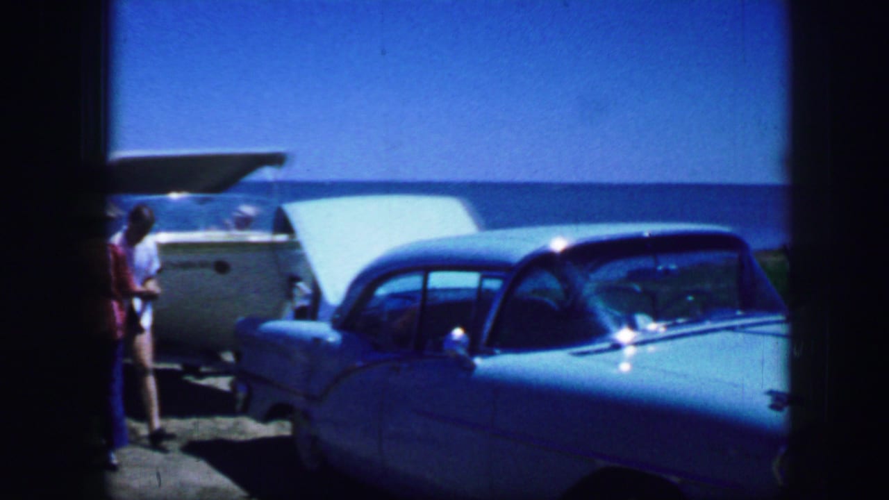 Light blue classic car beside a boat with a person partly visible at the left edge.