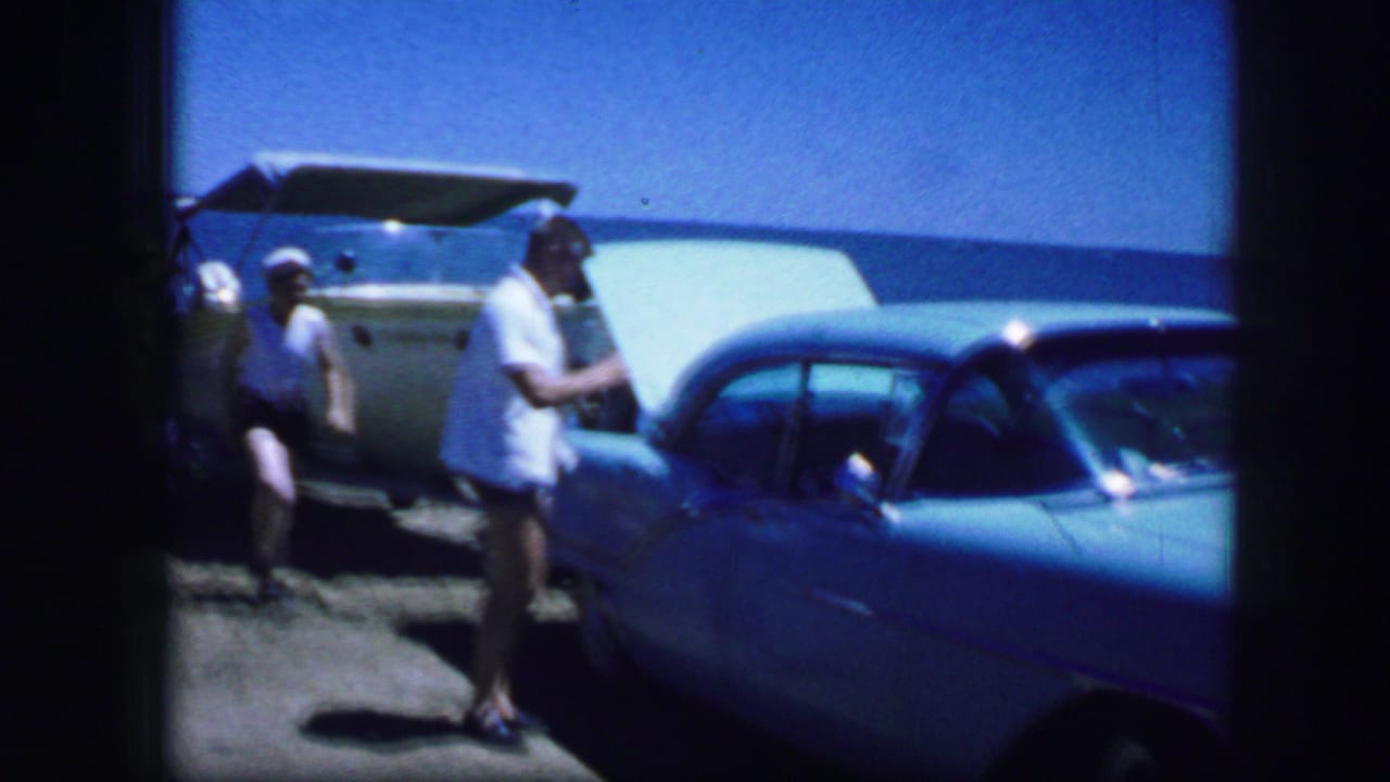 Fort Worth, Texas, 1964 home-movie frame showing adults near a blue classic car and a trailer or boat at a sunny roadside location.