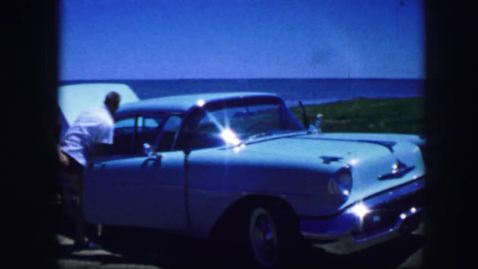 Fort Worth, Texas, 1964 frame showing a man in a white shirt near the front of a blue classic car with strong chrome glare.