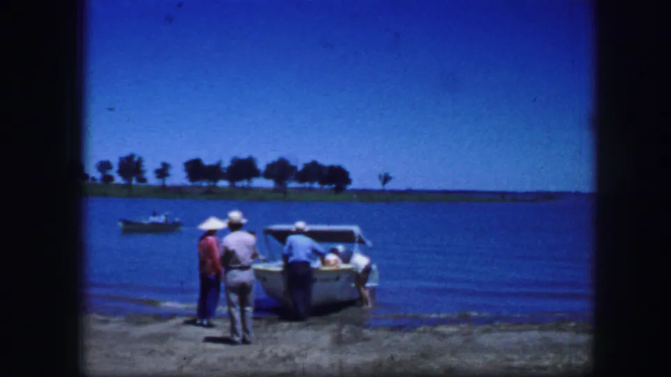 Home-movie frame from Fort Worth in 1964 showing men gathered beside a small boat on a lakeside concrete dock.