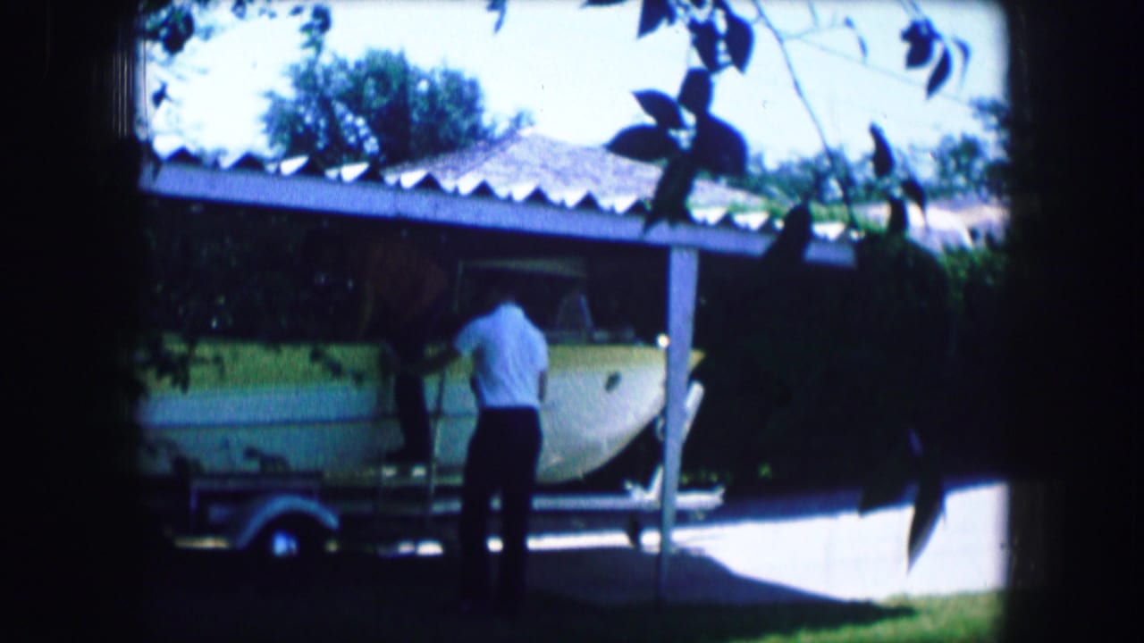 Man faces a small aircraft on a trailer with trees and carport shade around him.