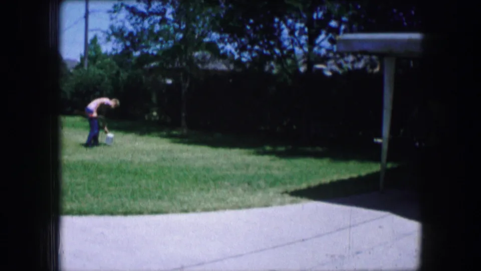 Adult figure tends to something on a sunny backyard lawn in Lewisville, Texas, home-movie footage from 1965.
