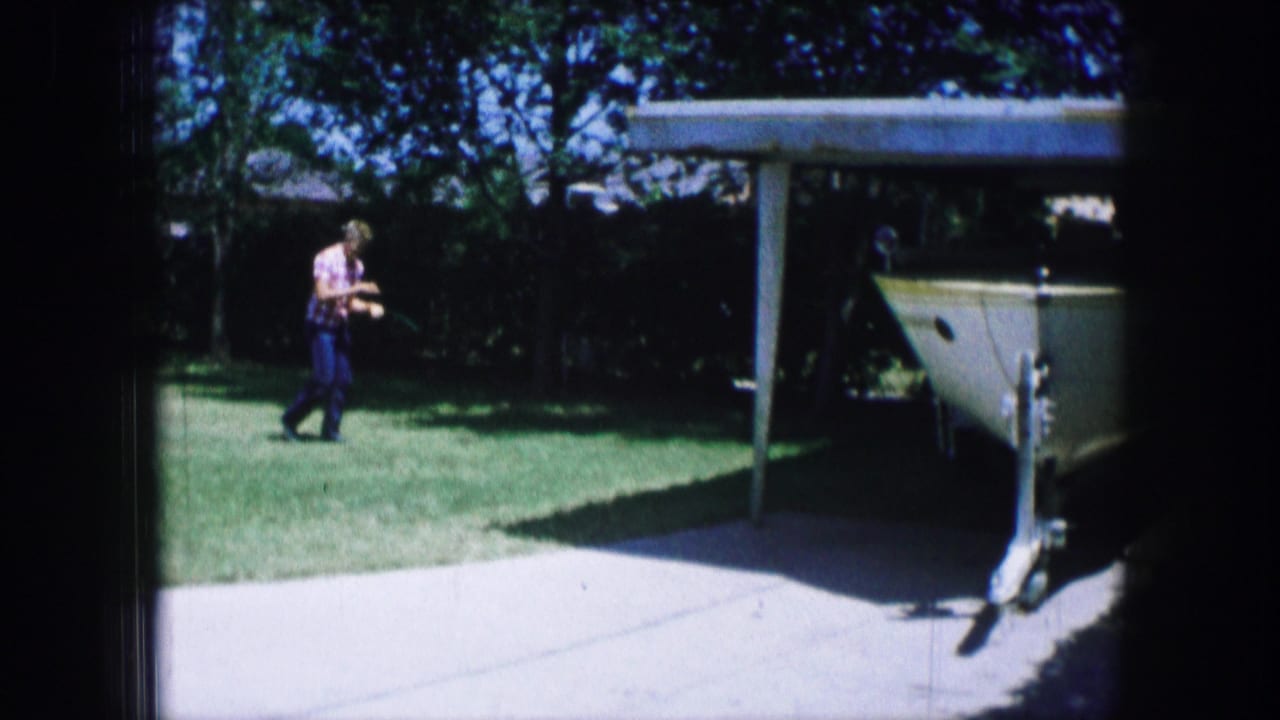 Man continues walking across grass with a white boat on a trailer at right.
