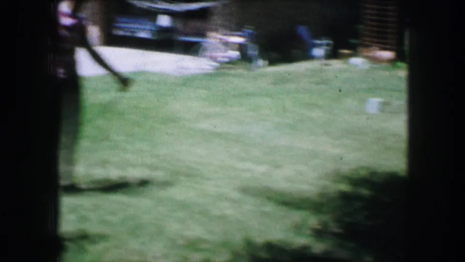 1965 Lewisville, Texas home-movie frame with motion blur as a bow passes across the lawn and bicycles remain visible near the driveway.