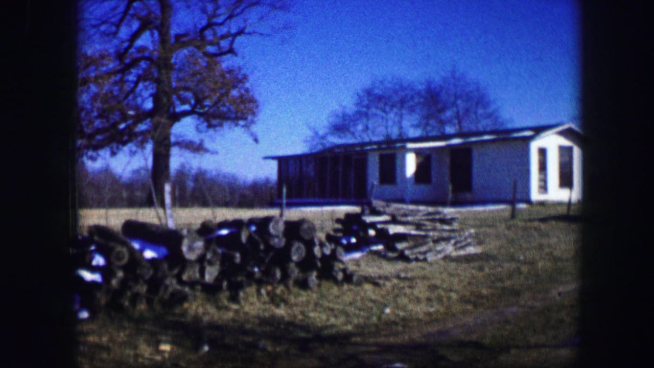 White hut beside a grassy rural yard with bare trees and dark equipment in the foreground.