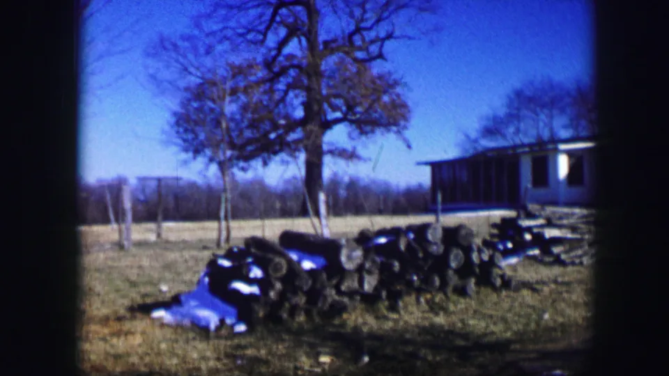 1967 Kirksville rural yard with dark equipment, a blue tarp, bare trees, fence posts, and a white hut at the edge of frame.