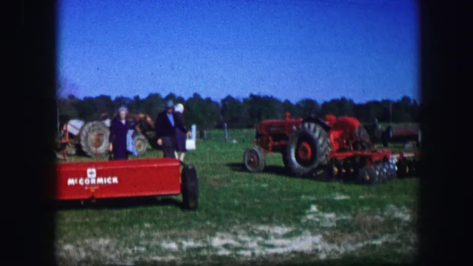 Adults at a Kirksville, Missouri rural fair appear near red McCormick equipment and tractors under a clear sky.