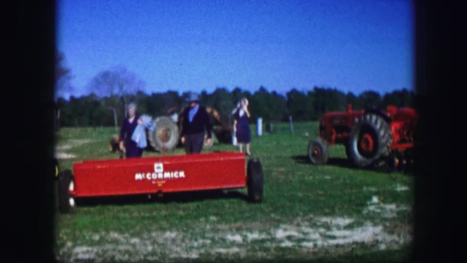 Kirksville fair visitors in 1967 stand near red McCormick equipment, tractors, and a large spool on a grassy display area.