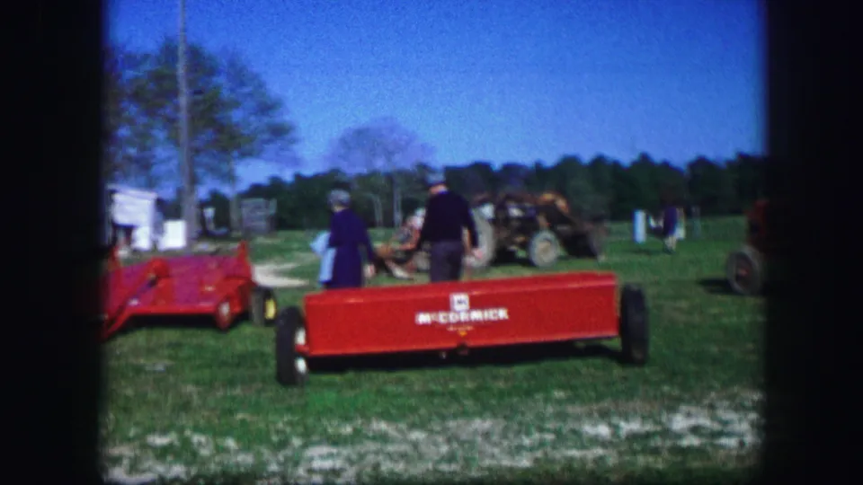 1967 Kirksville, Missouri frame with adults beside a red McCormick-marked trailer or implement, with white trailers and farm equipment in the background.