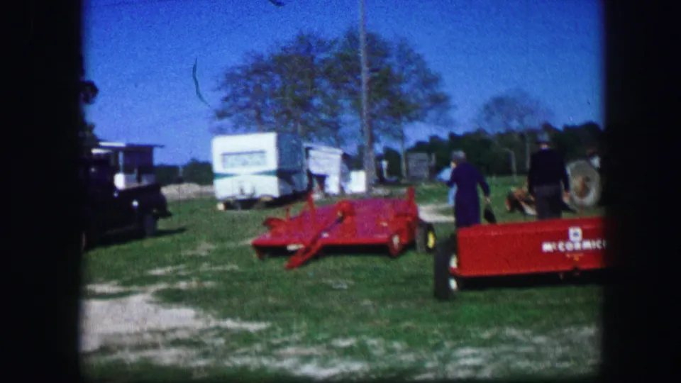 1967 Kirksville, Missouri frame with red equipment, a partially visible McCormick-marked trailer, adults, white trailers, and a dark truck in a grassy rural setting.