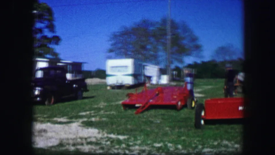 Rural campsite in Kirksville, Missouri, with a red farm implement, white trailers, black truck, grass, trees, and an adult standing nearby.