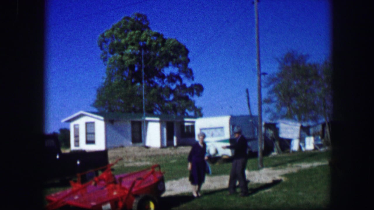 Two adults walk near a mobile home with a red toy car in the foreground.