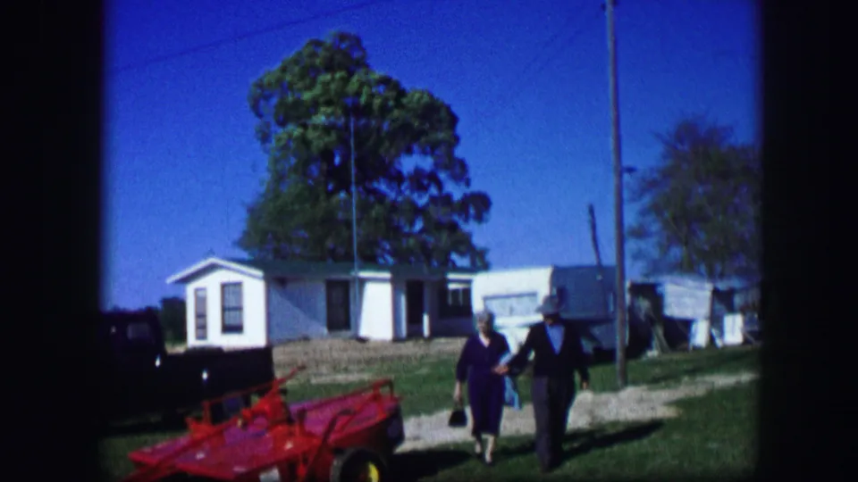 The pair walks closer to the camera in a 1967 Kirksville home-movie scene with a red toy car and trailers behind them.