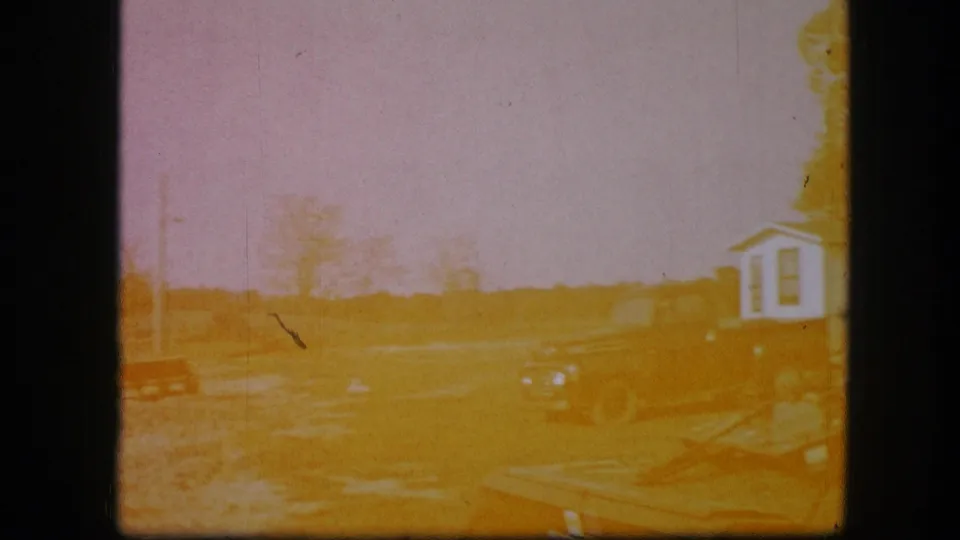 Near the end of the 1967 Kirksville clip, the farmyard remains visible beneath orange exposure shift, with a red implement and small white structure.