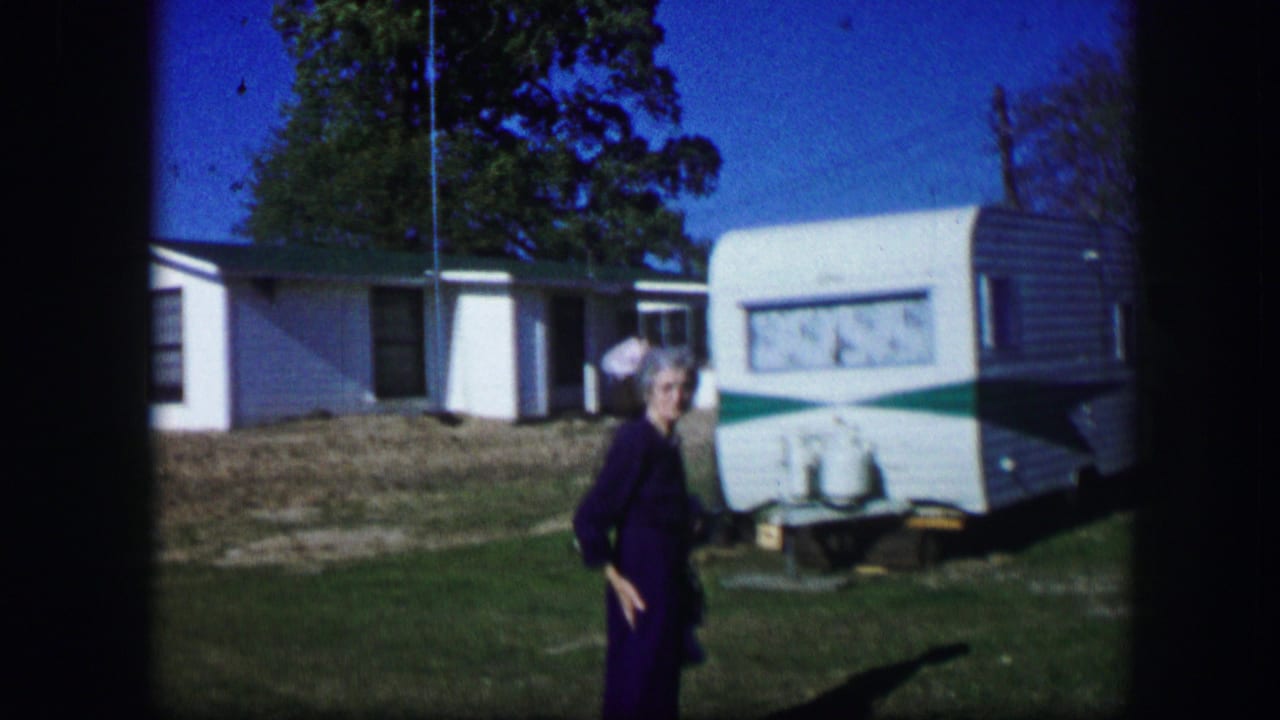 1967 Kirksville, Missouri home-movie frame showing a person in a yard beside a parked motorhome near a white house.