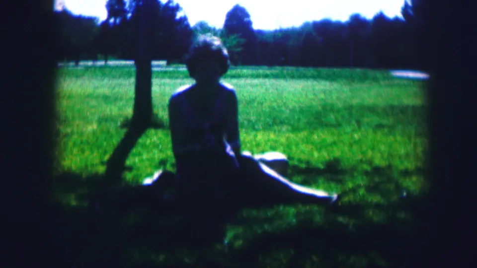 A 1967 Kirksville home-movie frame shows the seated woman and small dog in a bright park, partly silhouetted by backlight.