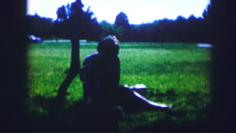 In this 1967 Kirksville frame, the woman bends slightly toward the small dog while seated under a tree in the park.