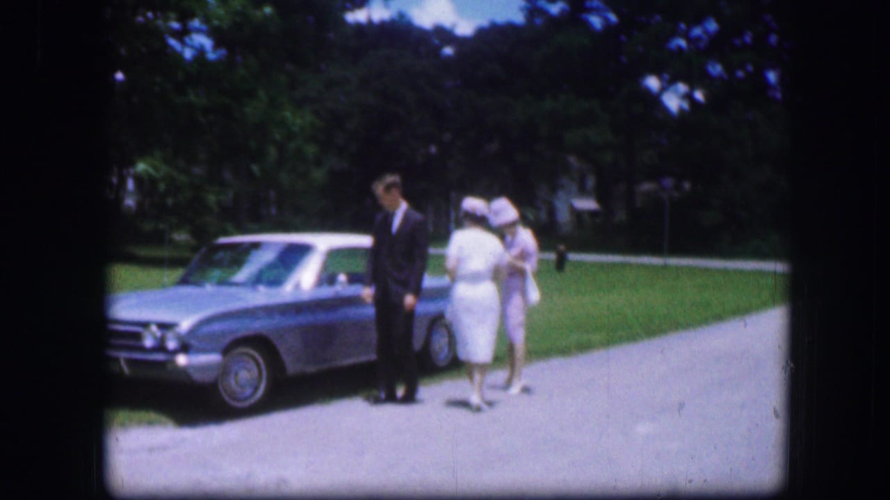 In 1967 Kirksville, Missouri home-movie footage, a suited man and two women in pale dresses stand by a light blue car outdoors.