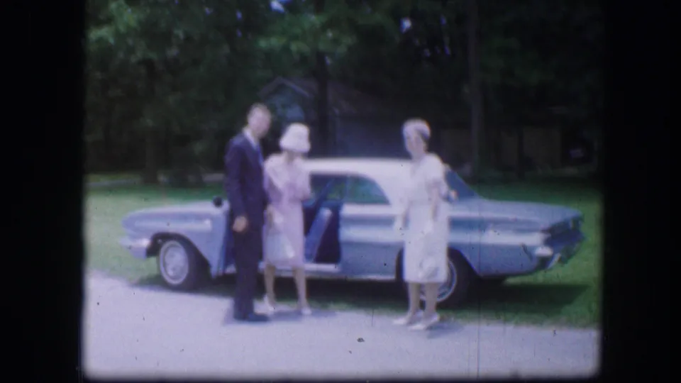 In Kirksville, Missouri, three adults pose outdoors beside a light blue car in 1967 home-movie footage.