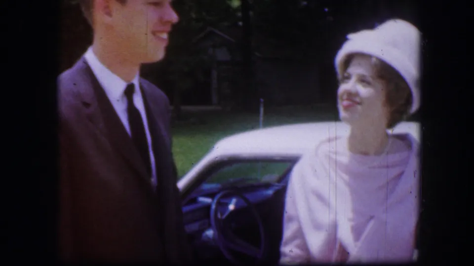 Close-up of a smiling man and woman beside a car during a 1967 outdoor home-movie scene in Kirksville.