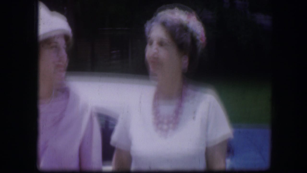 Two women near a blue car, one in a pale hat and another in a light dress.