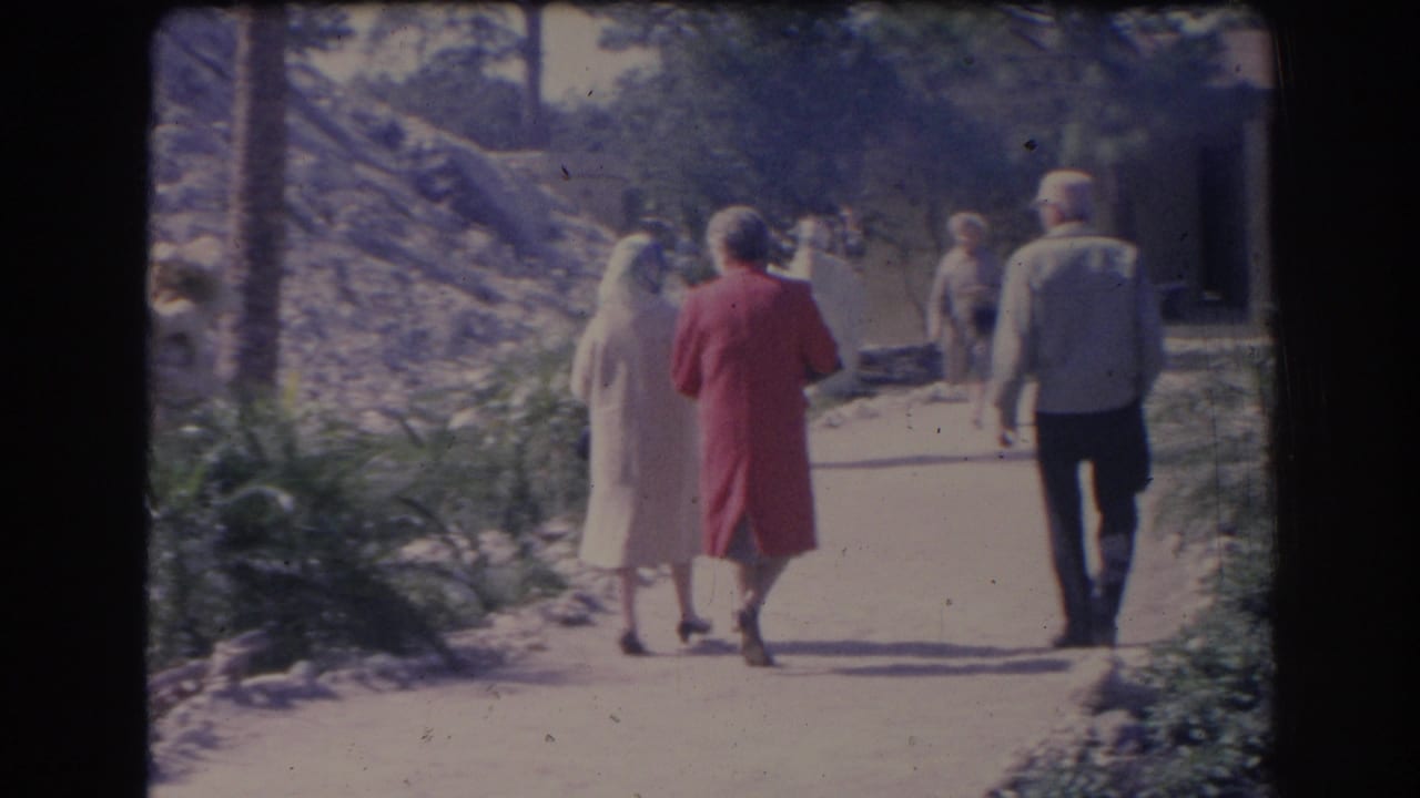 Adults walk away from the camera on a Sarasota sidewalk in 1969, including a woman in a red dress and a man in a light jacket.