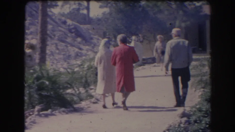 Adults walk away from the camera on a Sarasota sidewalk in 1969, including a woman in a red dress and a man in a light jacket.
