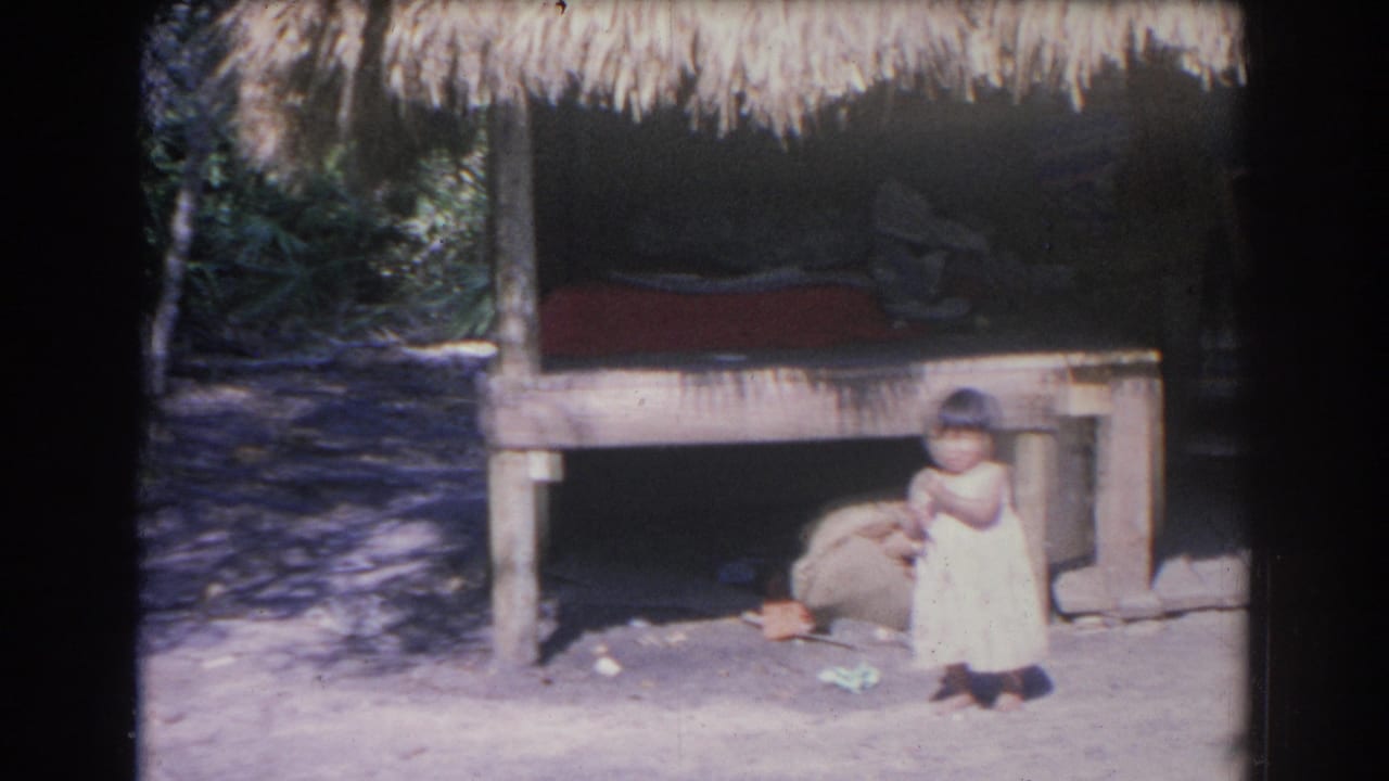 Small child standing near a thatched-roof structure in bright sunlight.