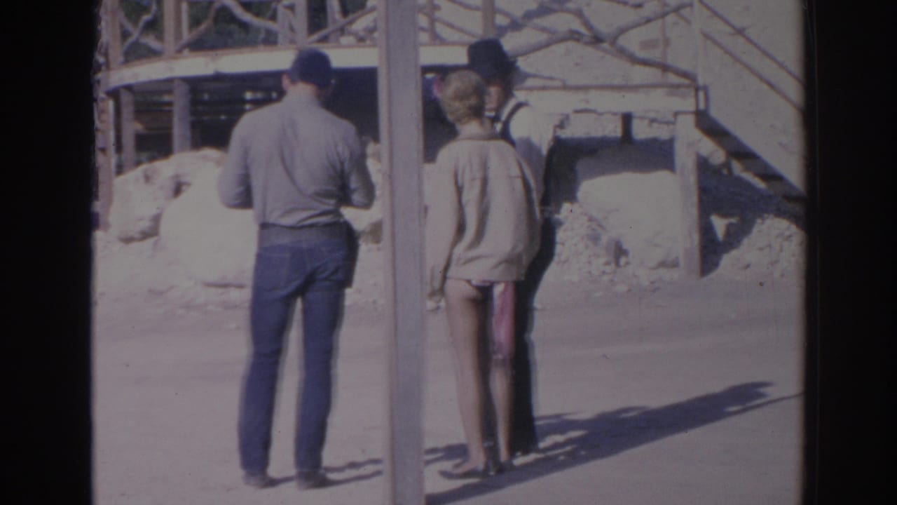 Two people stand near a post beside a rustic Western-style building front.