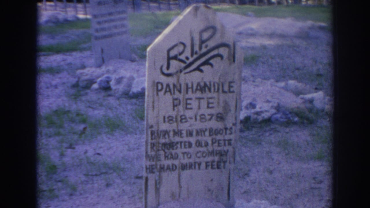 1969 Sarasota 8mm frame showing a weathered wooden grave marker for Pan Handle Pete with rocks, grass, and fencing behind it.