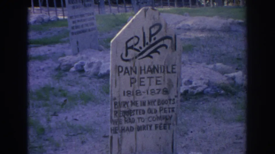 Close 1969 Sarasota frame of the Pan Handle Pete marker, with dark painted lettering, rough ground, stones, and fencing in the background.