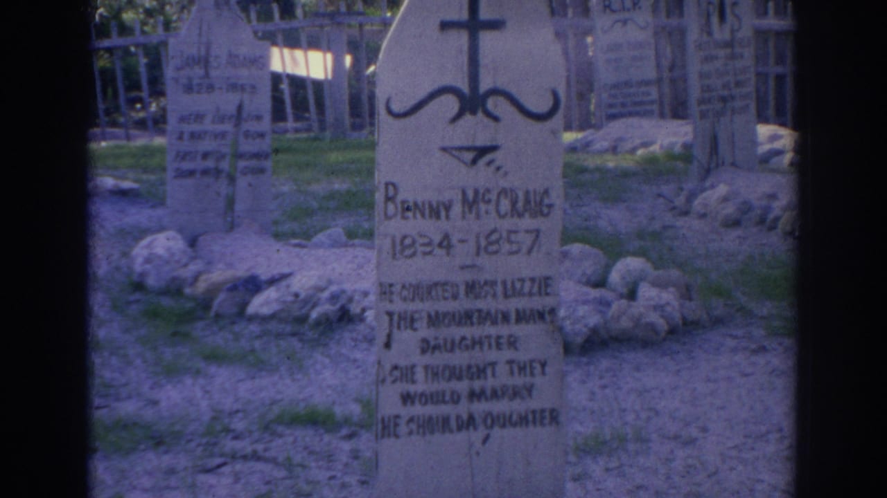 1969 Sarasota 8mm frame showing a wooden Benny McChang grave marker, a cross-shaped top, surrounding stones, grass, and other markers behind it.