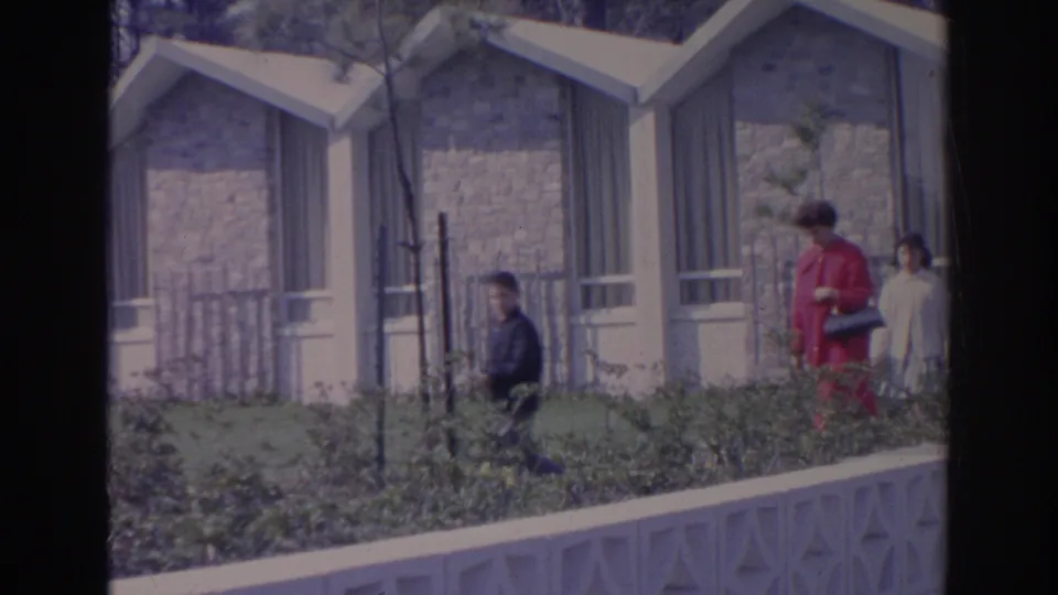 1969 Sarasota garden scene with distant visitors near small stone structures, fencing, and landscaped beds.