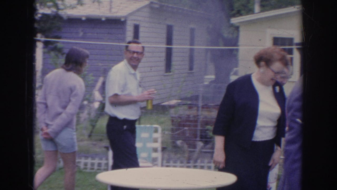 Adults gather in a 1969 Sarasota suburban yard, with a round table, fencing, trees, and house exteriors visible.