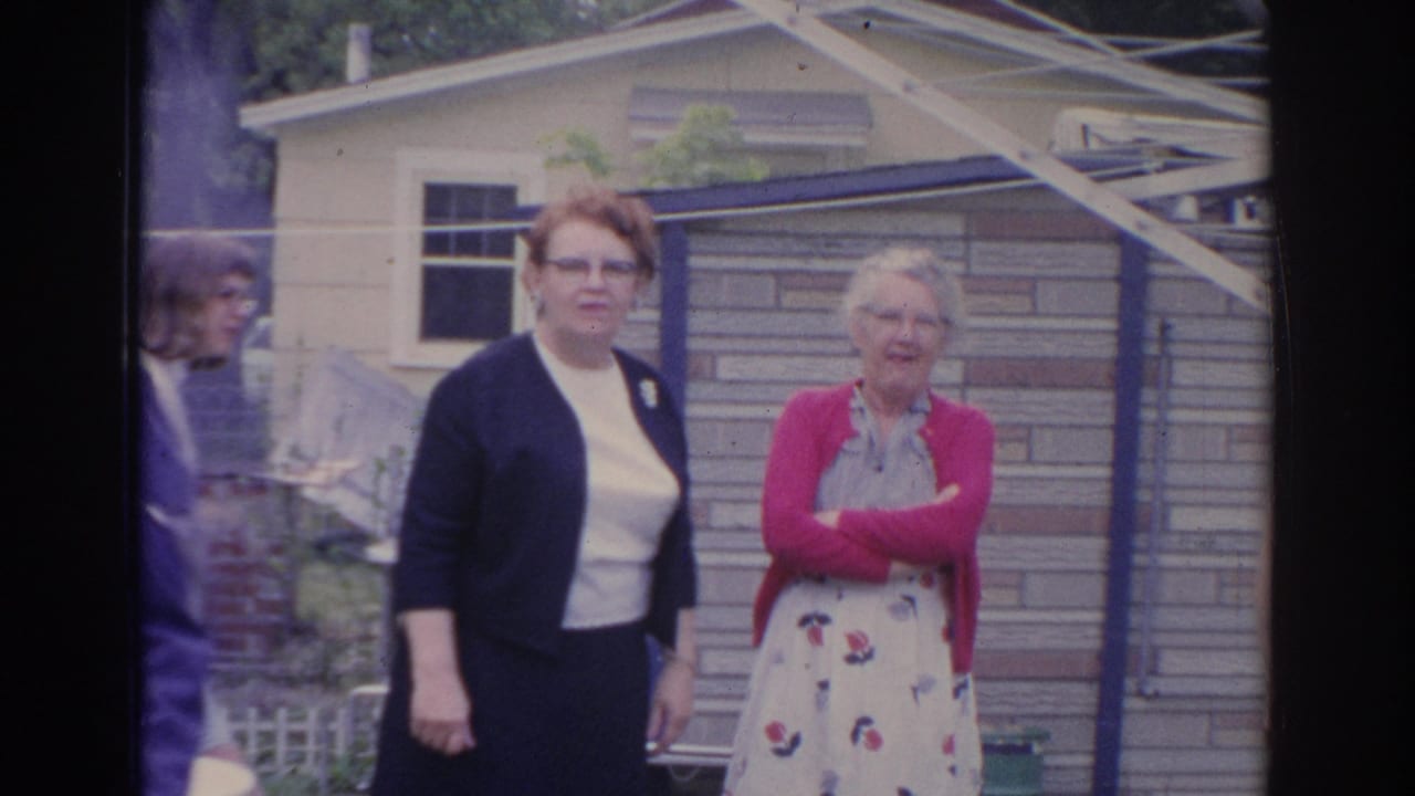 Two women stand near a shed while another adult is partly visible at the edge.