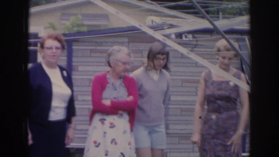 Several women stand together in a 1969 Sarasota backyard, with a shed, fence, and angled clothesline or support visible behind them.