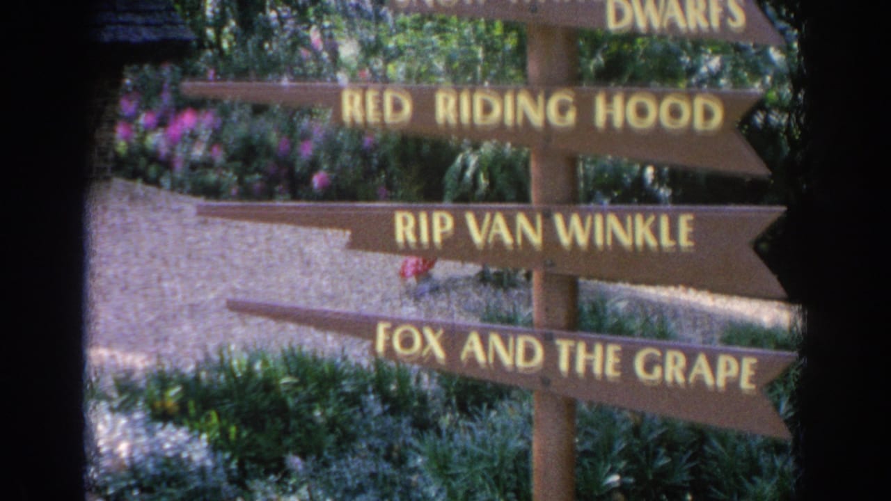 1969 Sarasota 8mm frame showing hand-painted storybook direction signs among foliage and pink flowers.