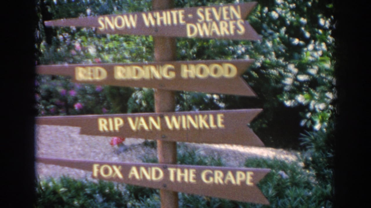 1969 Sarasota frame with wooden signs naming fairy-tale and fable scenes in a lush garden attraction.