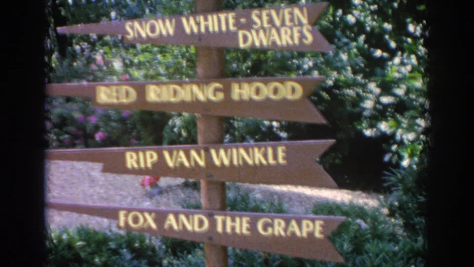 1969 Sarasota frame with wooden signs naming fairy-tale and fable scenes in a lush garden attraction.